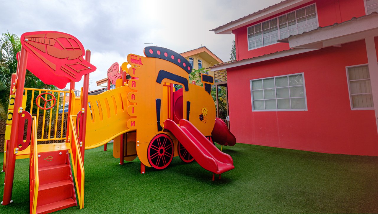 Camberley Loyang's custom train-shaped playground on the school's outdoor turf, with the red school building behind