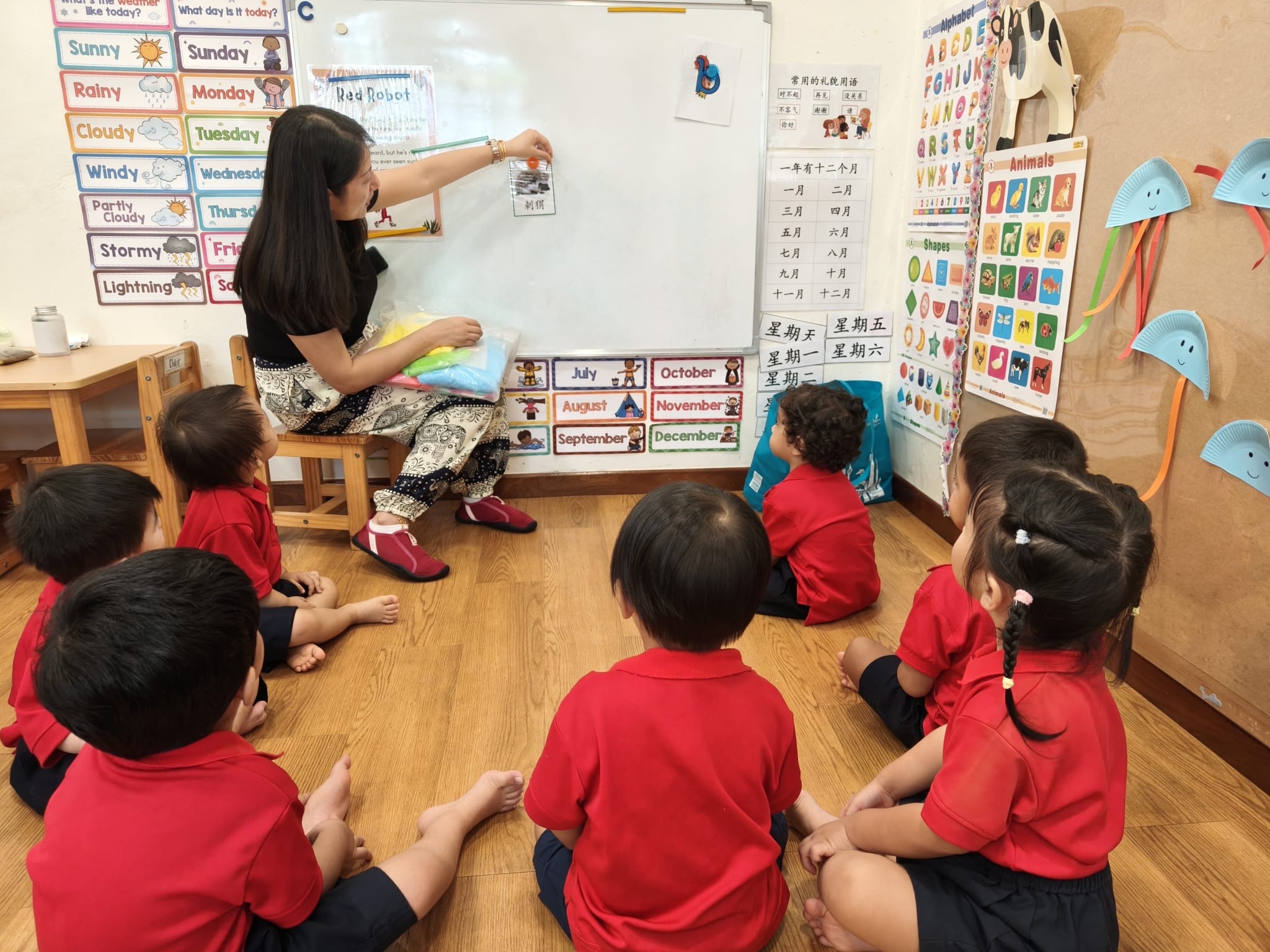 Teacher pointing to a Mandarin animal flashcard on the whiteboard while a small group of children sit and watch